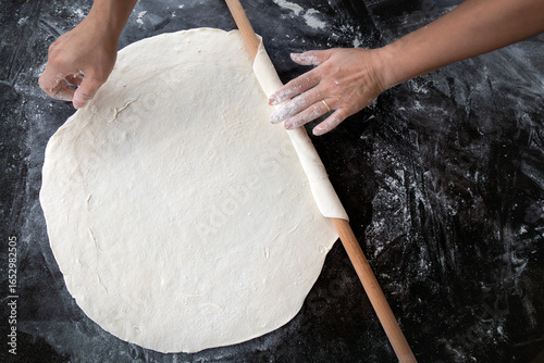 Hands rolling dough on a wooden table — traditional homemade cooking process