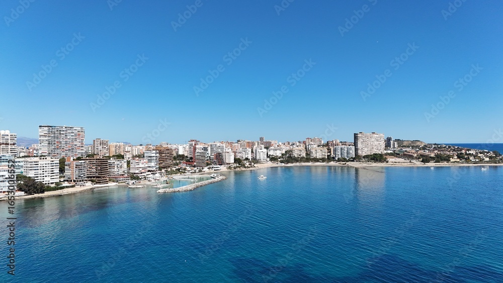 Obraz premium Panoramic view of a coastal city with modern buildings, sandy beach and clear blue sea under a bright sunny sky.