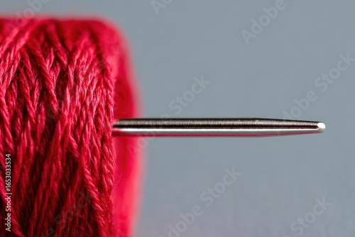 Red thread spool with a needle, close-up of sewing equipment on gray background