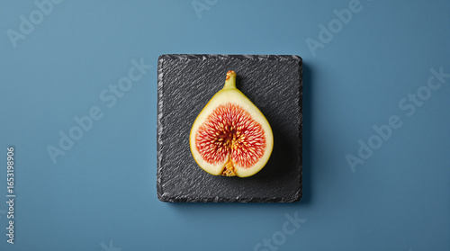 Fresh Cut Fig Half Placed on Black Slate Plate over Solid Blue Background for Culinary and Diet Project