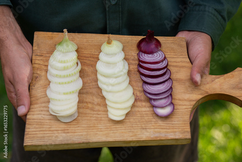Close-up image of male hands holding rustic wooden board with sliced yellow, red, white onions, fresh farm produce, natural ingredients, and healthy cooking preparation
