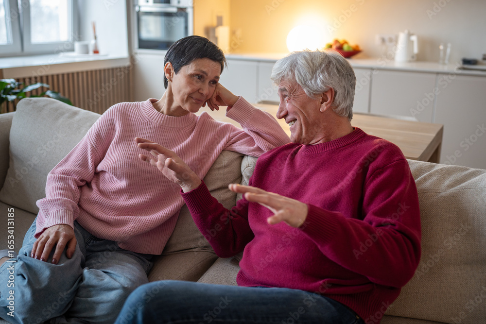 Fototapeta premium Senior husband enthusiastically shares memories, wife attentively listen. Elderly couple bonding storytelling, marital communication, joyful retirement, laughing spouses at home, family foundation