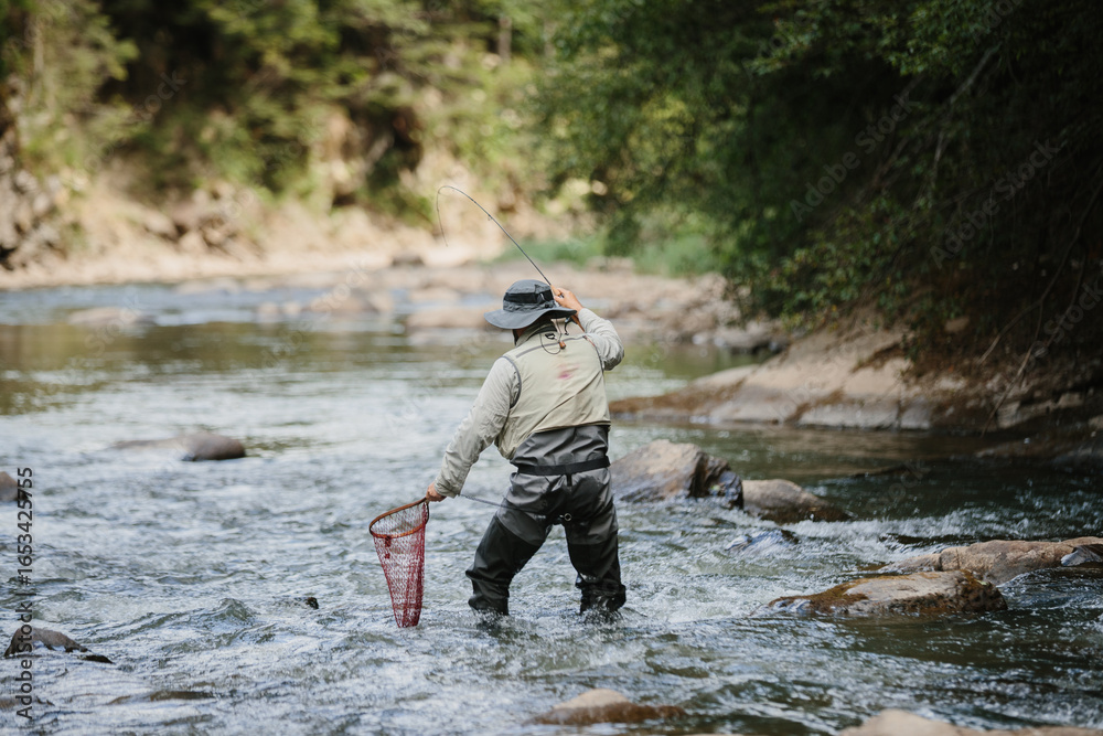 Obraz premium Fisherman catching trout in river with fishing rod and net