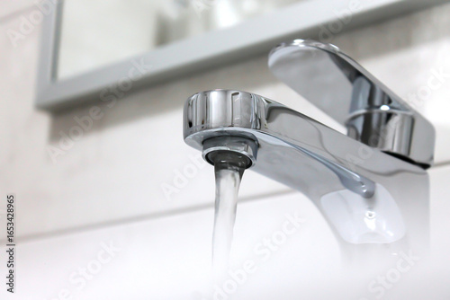 Running water from modern chrome faucet in bathroom sink close up interior view clean silver tap flowing liquid hygiene. Concept of plumbing water supply home maintenance.