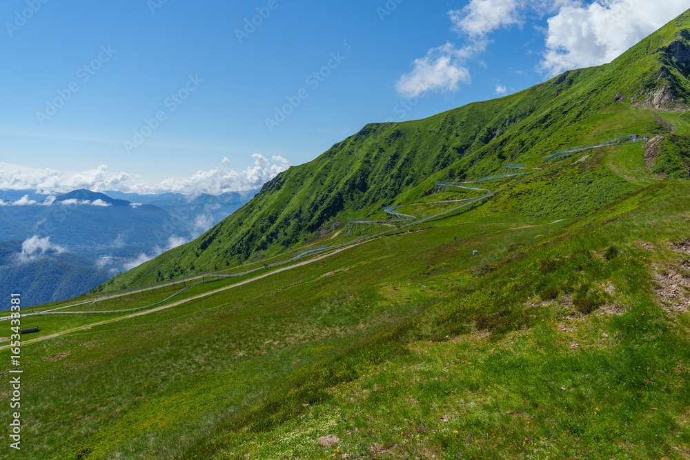Fototapeta premium serene winding road traversing the lush green hillside of the Swiss mountains under a bright blue sky with fluffy clouds and expansive mountain views