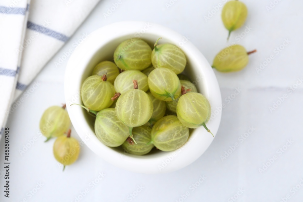 Fresh green gooseberries in bowl on white table, top view Fresh green gooseberries in bowl on white table, top view