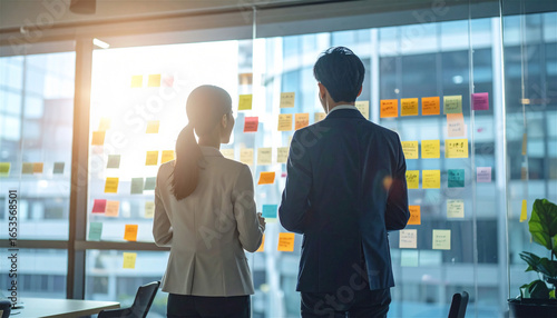 オフィスの会議室でビジネスパーソン男女が窓に貼られた多数の付箋を前にブレインストーミングやアイデア出しを行うチームワークの打ち合わせ