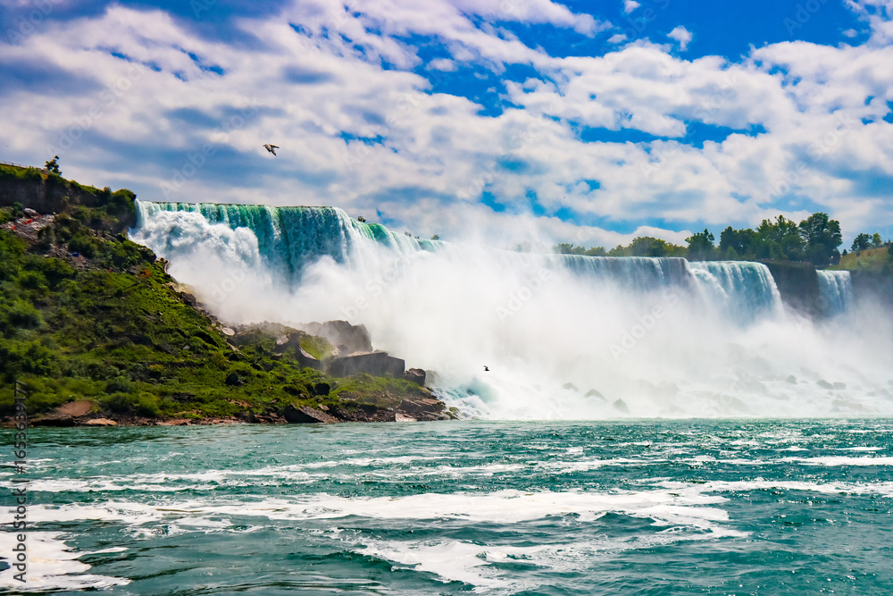 Obraz premium The gushing turquoise water from the Niagara falls with blue sky and white clouds the beautify scenry of nature