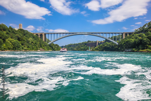 Fotografie The gushing turquoise water from the Niagara falls with blue sky and white cloud