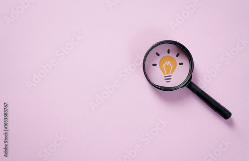 Bild auf Leinwand Magnifying glass revealing light bulb icon on pink background