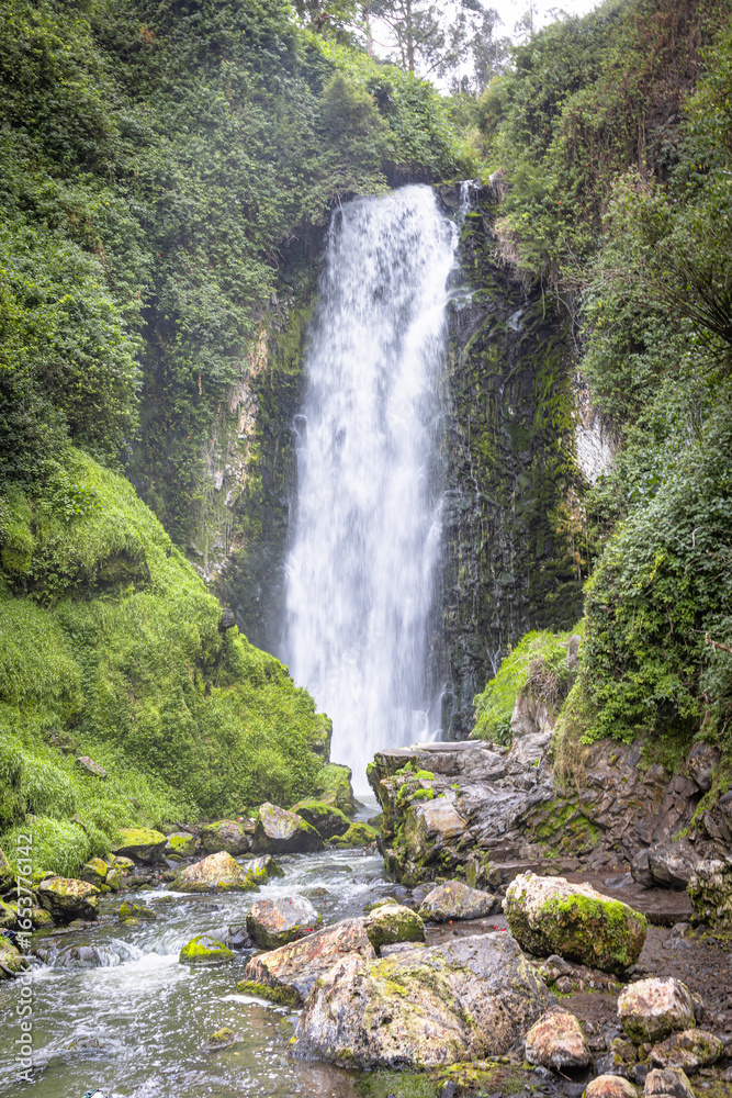 Obraz premium Majestic Peguche waterfall in Otavalo, Ecuador. Water cascades powerfully among moss-covered rocks and vibrant greenery, reflecting the purity of Andean nature.