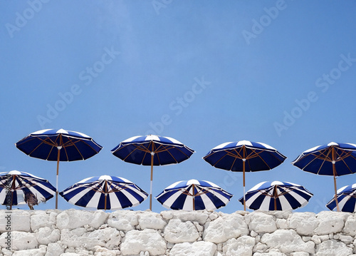 A series of blue and white striped umbrellas arranged on a white stone wall against a clear blue sky.
