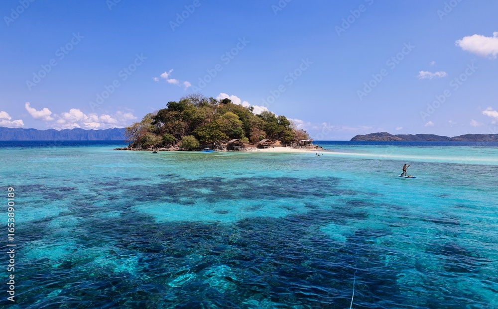 Fototapeta premium Tropical island with clear turquoise waters and paddleboarder.