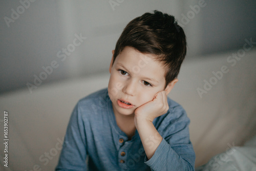 A preschool boy in a blue T-shirt is boring