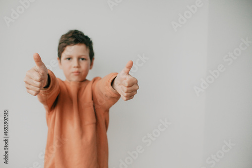 A preschool boy on a light background shows a thumbs up