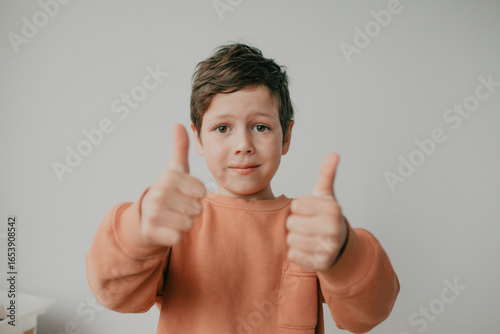 A preschool boy on a light background shows a thumbs up