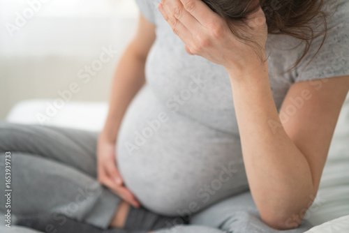 Fotografi Expecting mother holding her head in pain while resting on bed