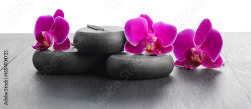 Acupuncture needles, orchid flowers and spa stones on grey wooden table against white background, closeup