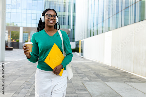 Smiling black student walking with coffee and books in university campus