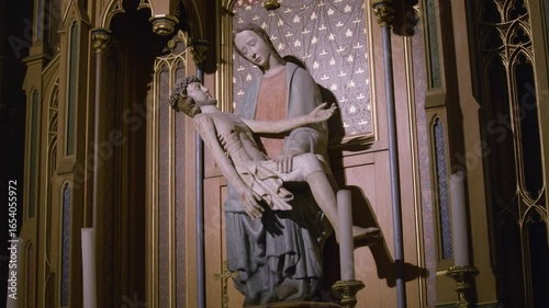 Stone religious statue of Mary and Christ inside a gothic church with wooden altar and candles. Tilt shot of sculpture composition:  the Virgin Mary holding the body of Christ