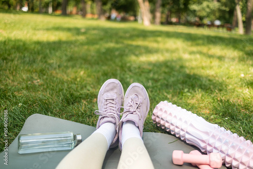 Sports shoes sneakers, dumbbells, yoga mat and bottle of water on fresh green grass. Sport equipment pov view. Concept healthy lifestyle, sport and diet.