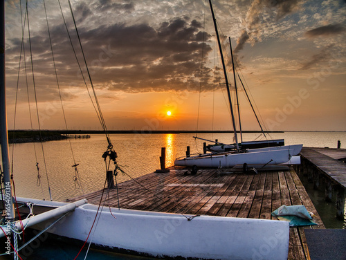 Scenic sunrise and blue hour at Breitenbrunn, Lake Neusiedl, Austria. Sailboats moored at a wooden pier with dramatic clouds, calm water, and golden light symbolizing travel, nature, and tranquility.