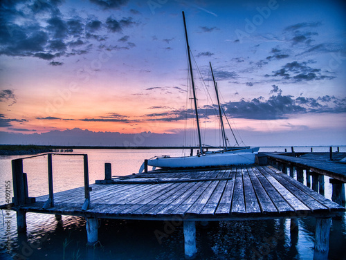 Scenic sunrise and blue hour at Breitenbrunn, Lake Neusiedl, Austria. Sailboats moored at a wooden pier with dramatic clouds, calm water, and golden light symbolizing travel, nature, and tranquility.