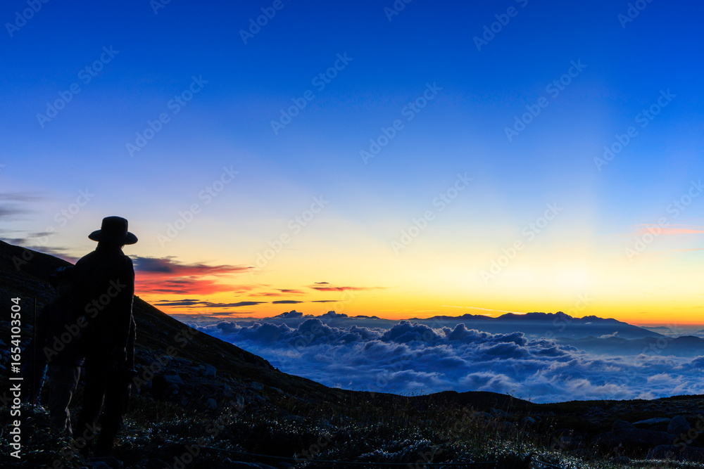 Fototapeta premium 雲海と夜明け前の空を撮影する登山者のシルエット