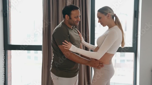 A man kisses a pregnant woman's belly and they hug and hold hands