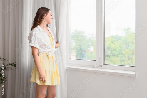 Young woman opening light curtain in room Free Download Young woman opening light curtain in room - GFXLoad