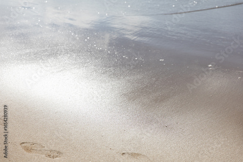 Ocean water on beach sea sand with sun reflection with footprints