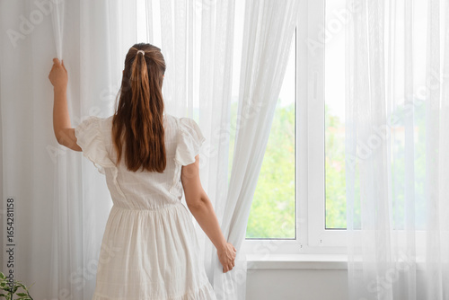 Free Download Young woman opening light curtain in room, back view - GFXLoad