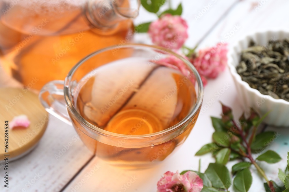 Tasty rose tea in glass cup, flowers and leaves on white wooden table, closeup Tasty rose tea in glass cup, flowers and leaves on white wooden table, closeup