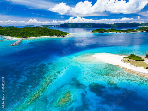 青い海の白砂のビーチが美しい無人島、嘉比島のドローン撮影（沖縄県島尻郡慶良間諸島座間味島嘉比島）
島には白い灯台がある。
座間味島や渡嘉敷島、阿嘉島も見えている。