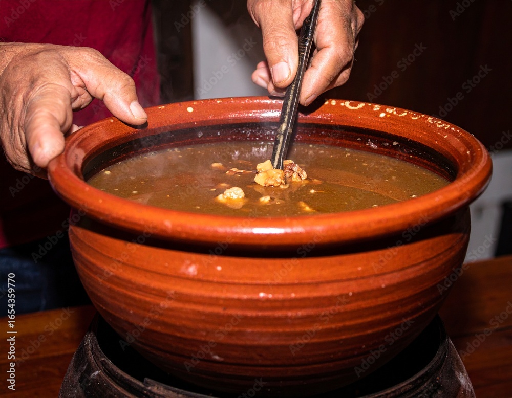 Fototapeta premium A person stirring a savory broth with chopsticks in a rustic ceramic bowl.