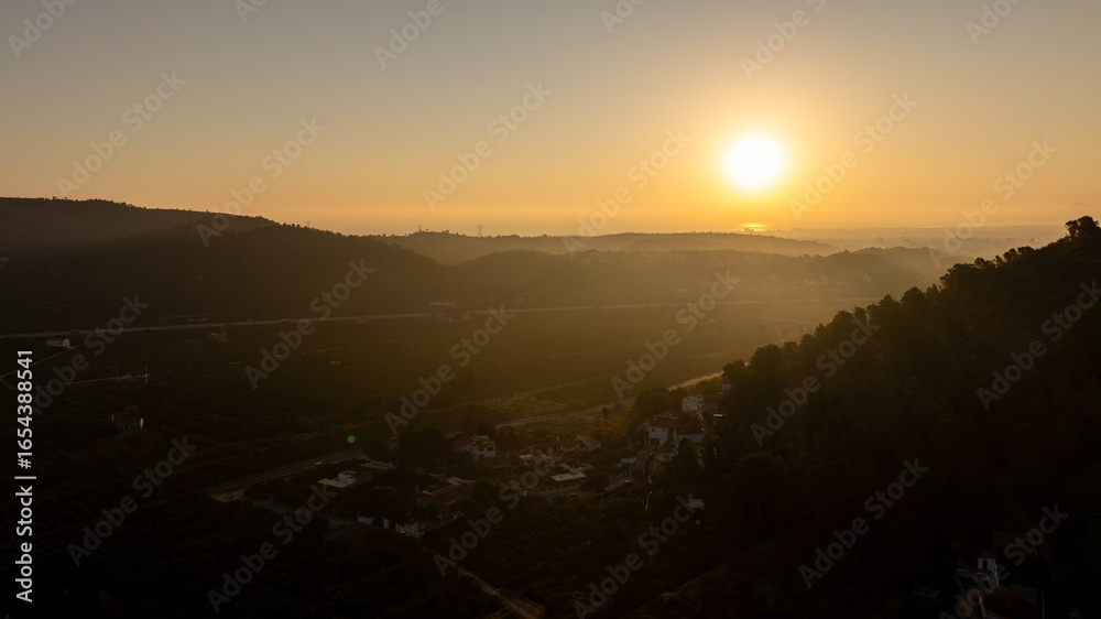Obraz premium Golden sunrise casting long shadows over the rolling hills, lush orchards, and serene landscapes of Gandia, Spain, creating a picturesque morning scene