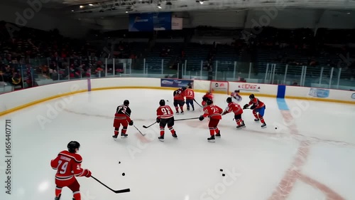 Watch the youth hockey players battle for the puck in this competitive ice hockey game with teams sporting red and blue jerseys.