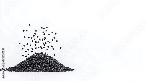 Small black seeds falling onto a pile against a white background