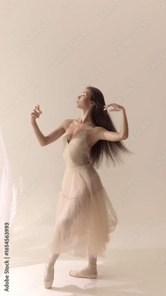 Fototapeta premium Graceful dancer in beige dress spraying perfume with flowing motion. Concept of beauty, perfume elegance, creative expression, femininity, health, wellbeing, and authentic lifestyle.
