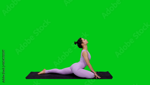 Young woman in bodysuit doing pigeon pose while practicing yoga on green chroma key background