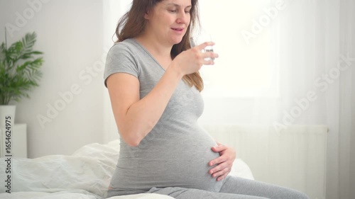 Expecting mother taking mindful sip from glass, maintaining hydration during pregnancy. Soft natural light enhances this health-conscious moment at home.