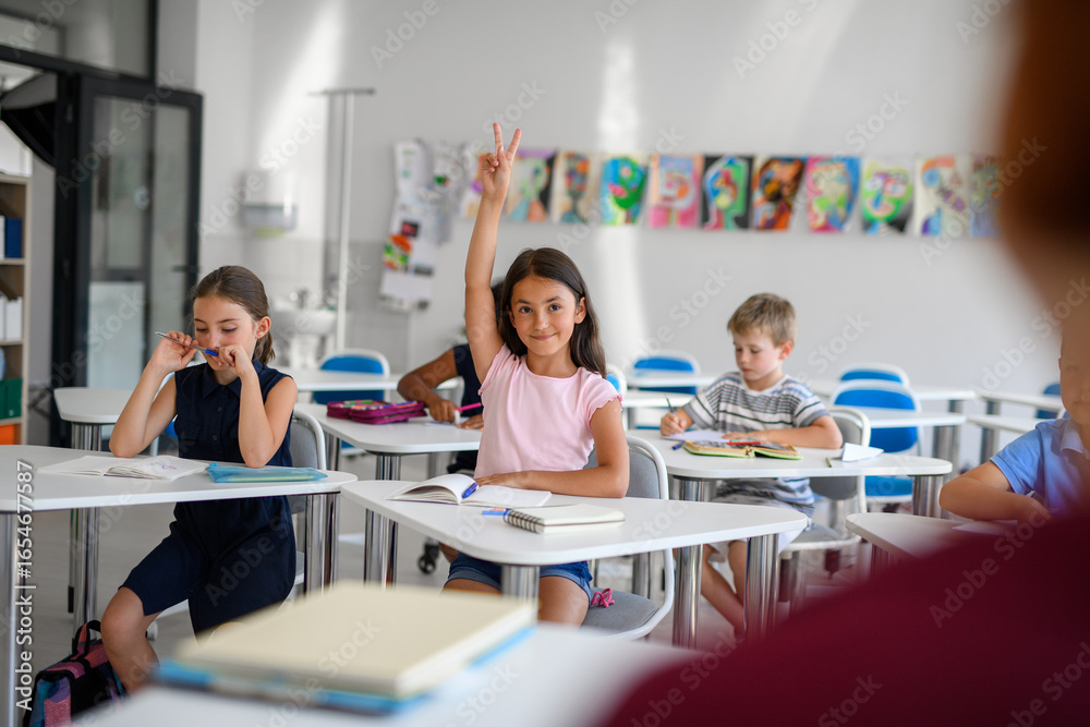 Fototapeta premium School children sitting at the desk in classroom on the lesson, raising hands.