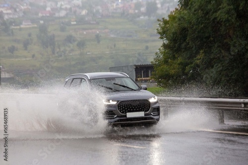 A car drives on a road flooded by rain. Heavy rainfall, climate change.