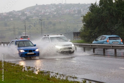 A car drives on a road flooded by rain. Heavy rainfall, climate change.