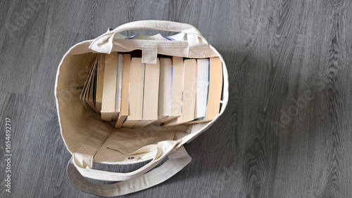 overhead view of open canvas bag of 11 books sitting on a gray wood floor