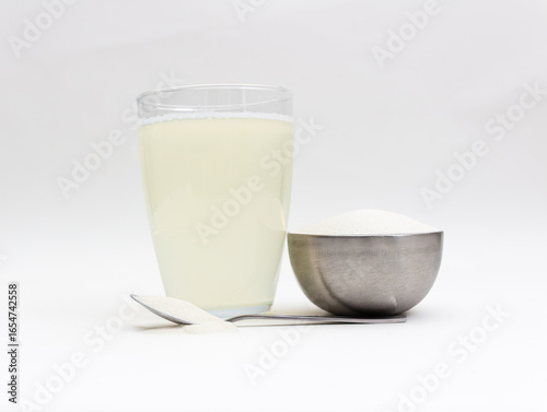 Spilled, dry collagen powder in metal container and spoon next to liquid, dissolved collagen in front of background. Version 10.
