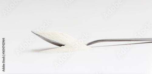 Dry collagen powder is spilled out from spoon in front white background. Version 5.