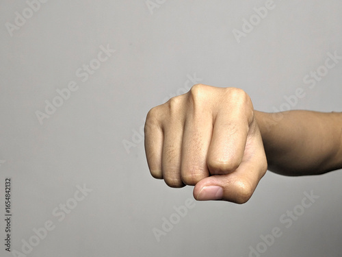 Fotografie Close up of a person's fist punching forward in a clear, neutral studio setting against a grey background emphasizing the hand and its impact
