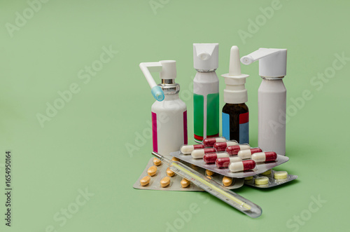 medical treatment with pills, sprays, and thermometer on green background