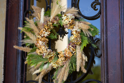 Autumn wreath made of dried hydrangea flowers, pampas grass and pine branches hanging on rustic wooden door. Cozy seasonal home decor, countryside atmosphere, vintage style and handmade craft